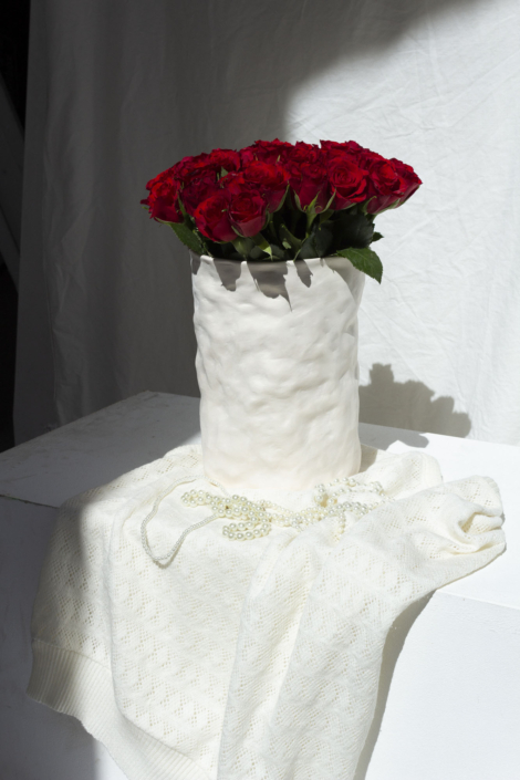 Foto zeigt zylindrische Porzellan-Vase mit unebener Oberfläche, die mir roten Rosen bestückt ist