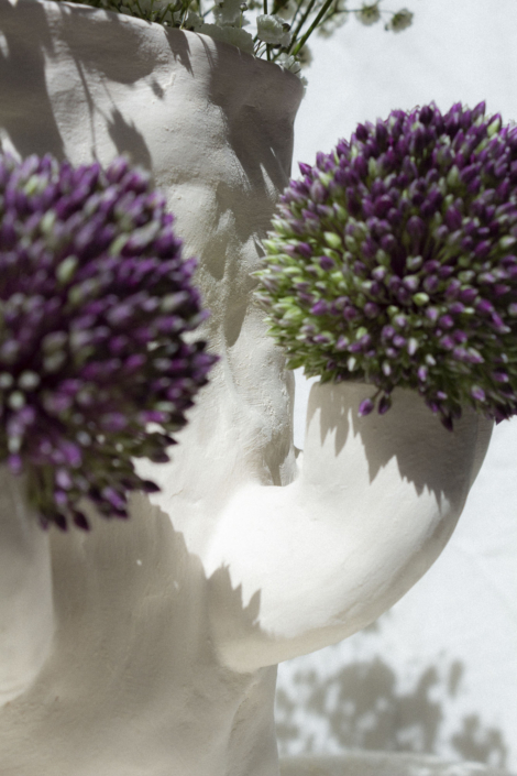 Foto zeigt eine Detailaufnahme einer Porzellan-Vase mit Armen, in der Blumen stecken