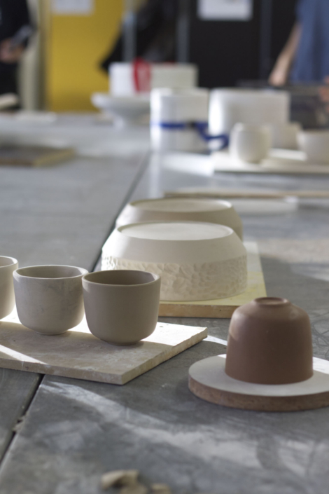 Foto zeigt Claymodell einer Tasse und die davon gefertigten Abgüsse. Im Hintergrund sind unscharf weitere Entwürfe und Gipsformen zu sehen.