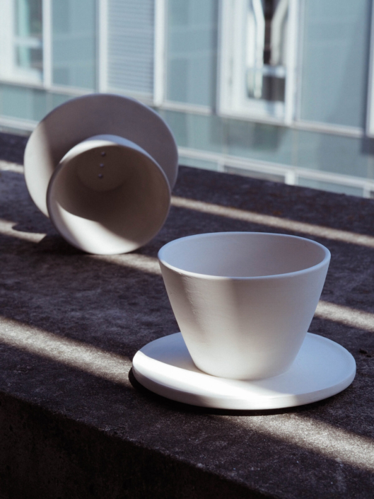 zwei Keramische Kaffeefilter, einer stehend, einer liegend in gestreiftem Licht