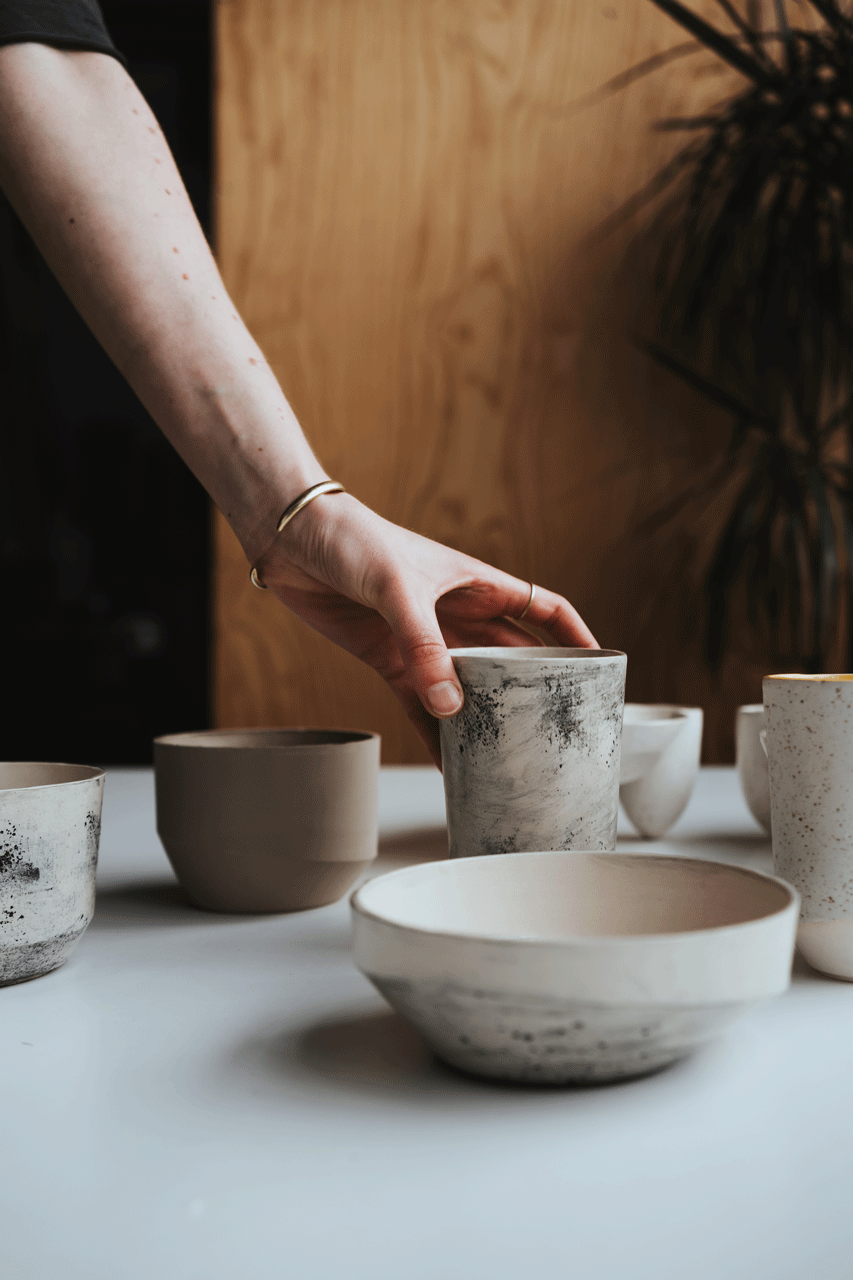 Hand greift nach einer Tasse, die zwischen anderen Keramikstücken steht