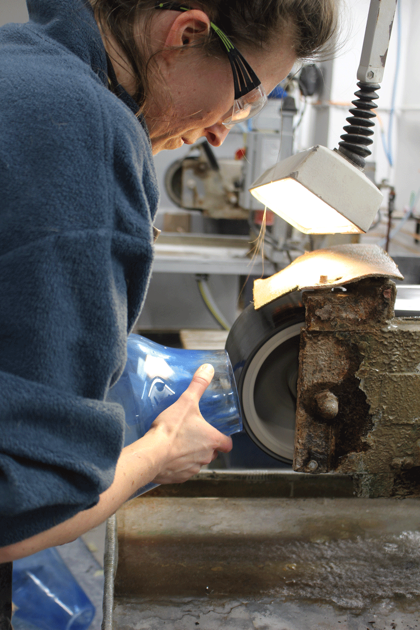 Maike hält ein blaues Glasobjekt an ein Schleifband