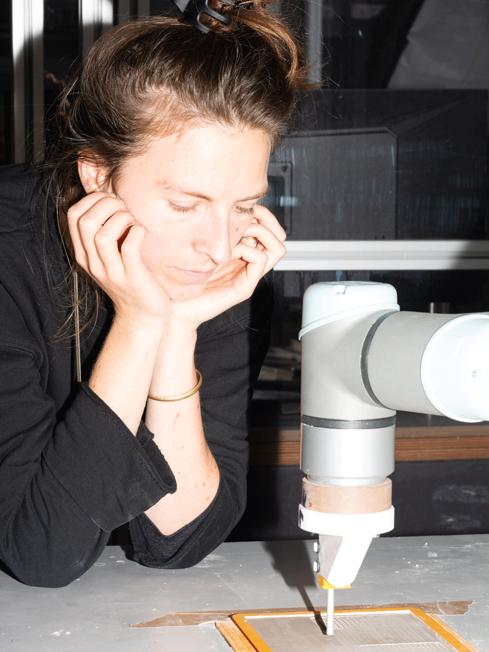 Mensch hat den Kopf auf Hände gestützt und beobachtet, wie ein Roboterarm Ton stempelt und so strukturiert