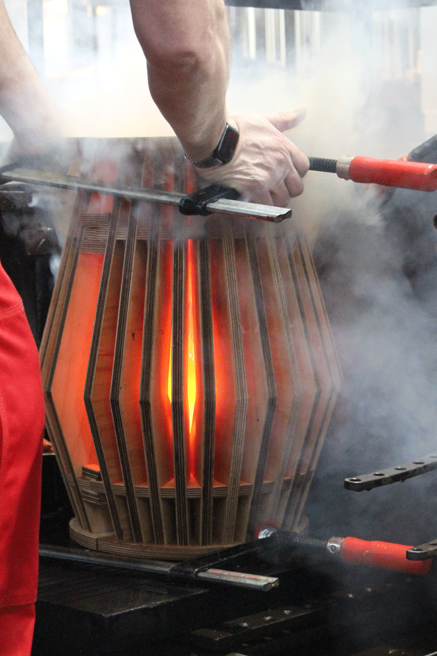 Holz zeigt glühendes Glas in einer Spantenform, aus der es stark qualmt