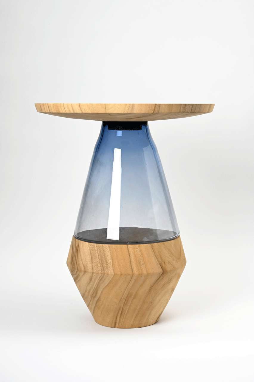 Tisch aus einem Holzfuß und einer Holzplatte bestehend, zwischen denen ein Glasobjekt den Grundkörper vervollständigt